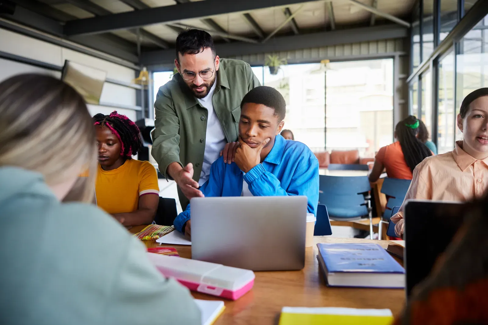 Teacher helping a student on a laptop at a cafeteria table