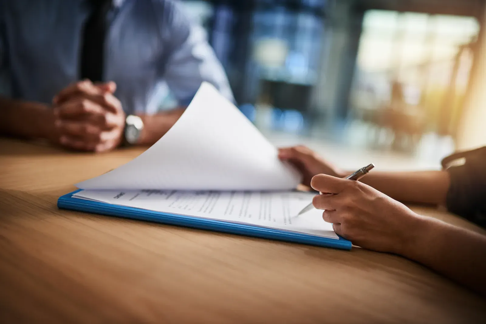 Paperwork stacked on an office desk beside a pen, ready for signatures