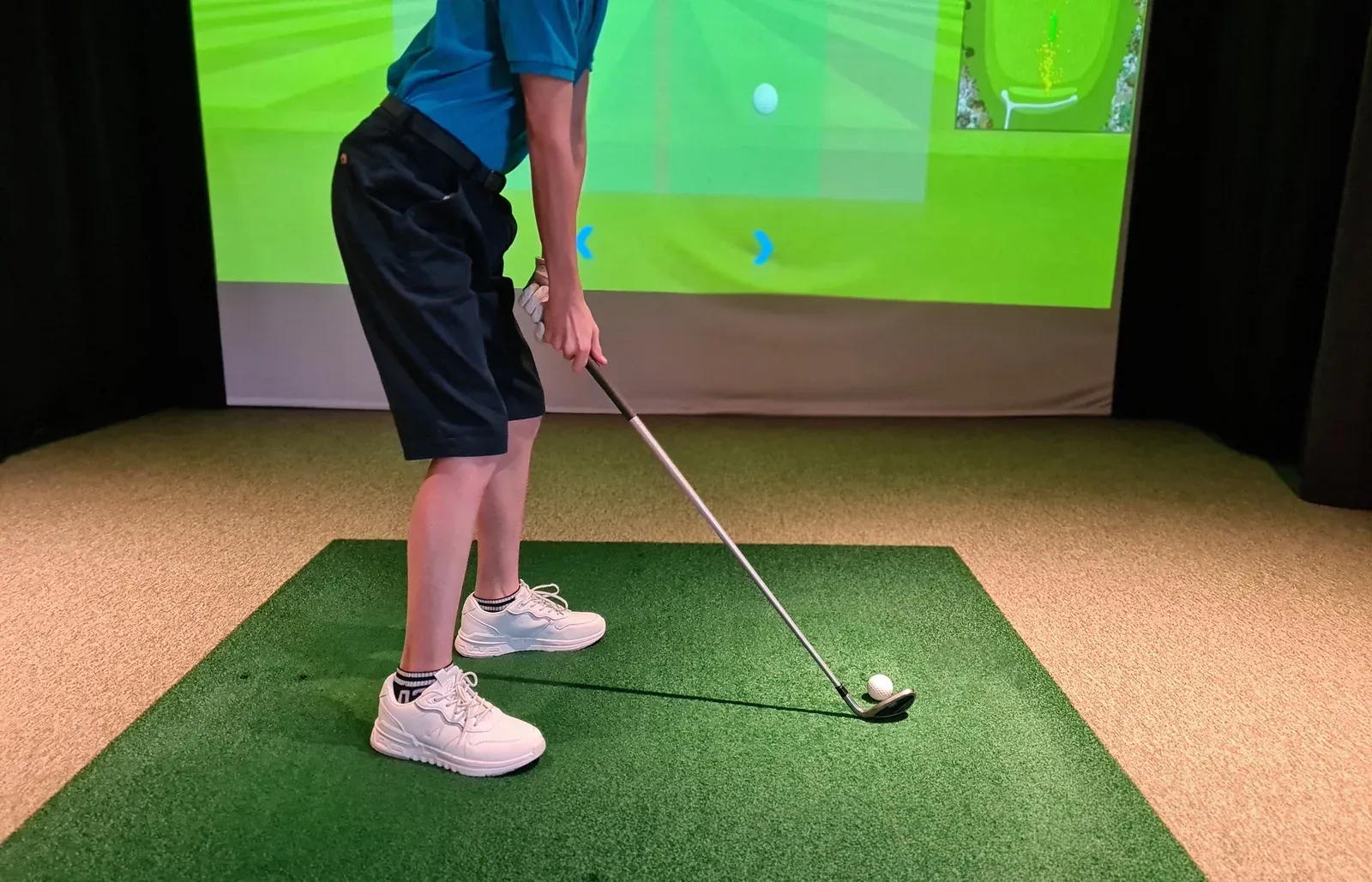 A golfer addressing a shot on an indoor golf simulator screen