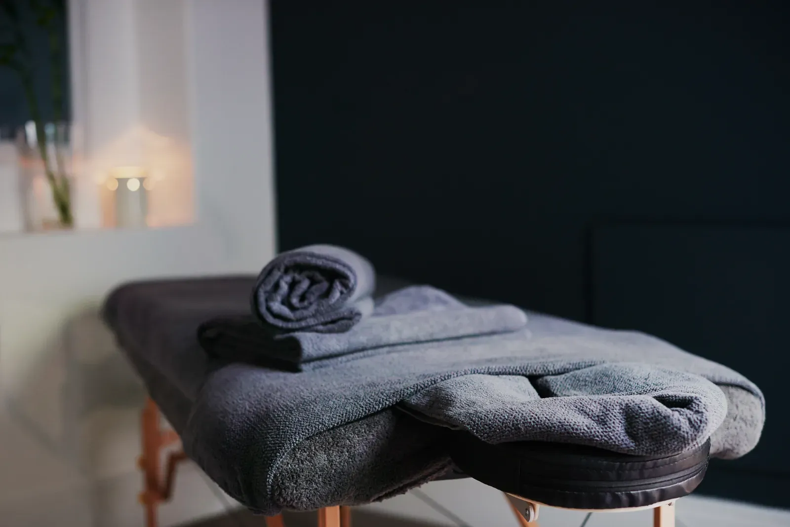 A padded massage table waiting in a calm treatment room beside a stack of folded linens