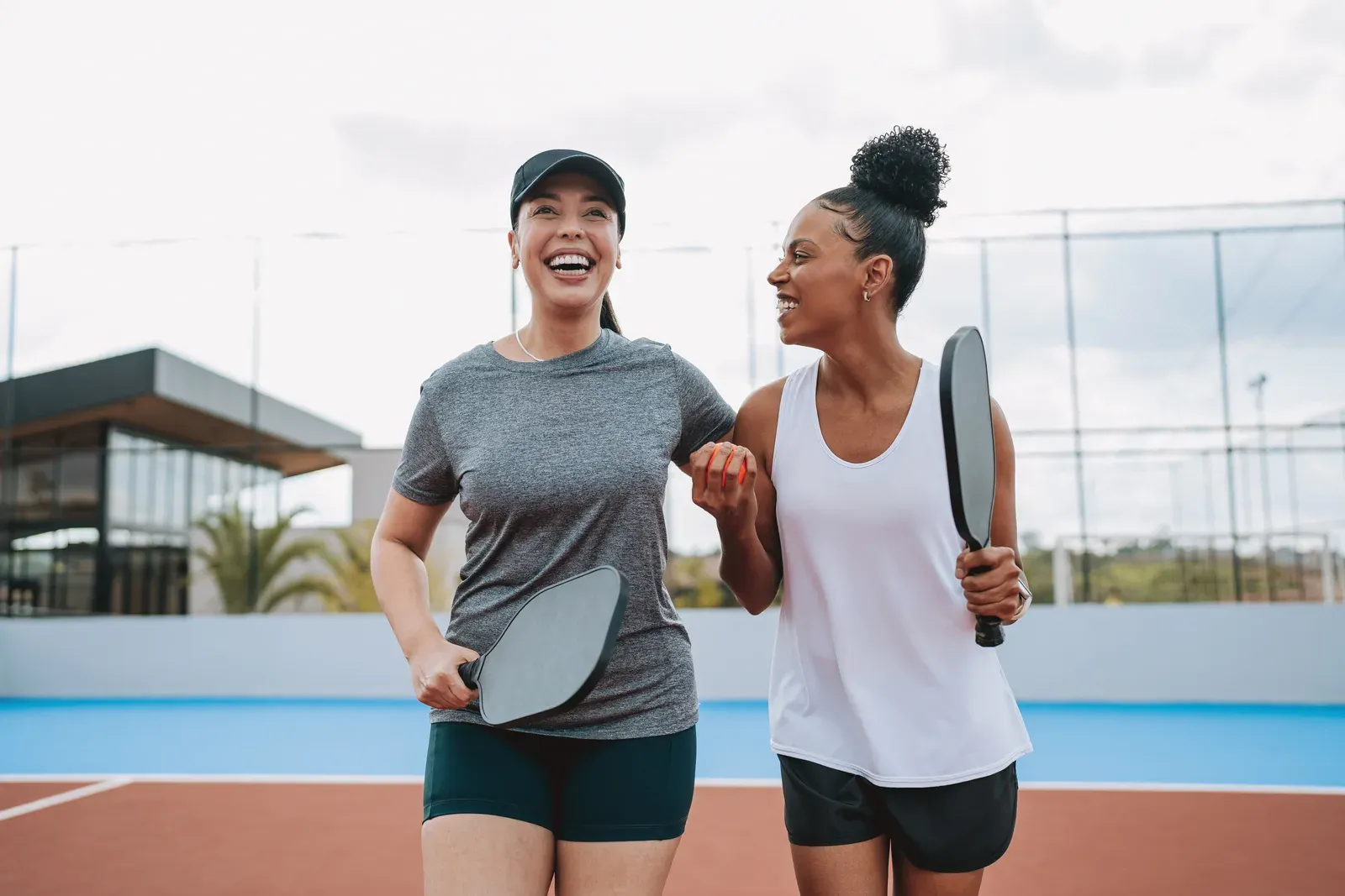 Two smiling women carrying paddles as they walk off an outdoor court