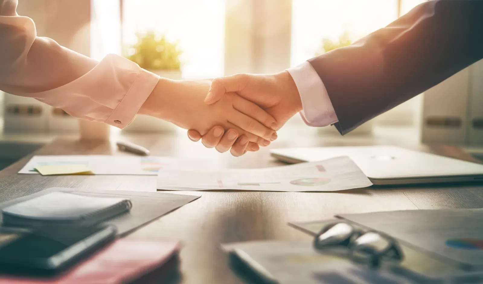 Two people shaking hands across an office desk