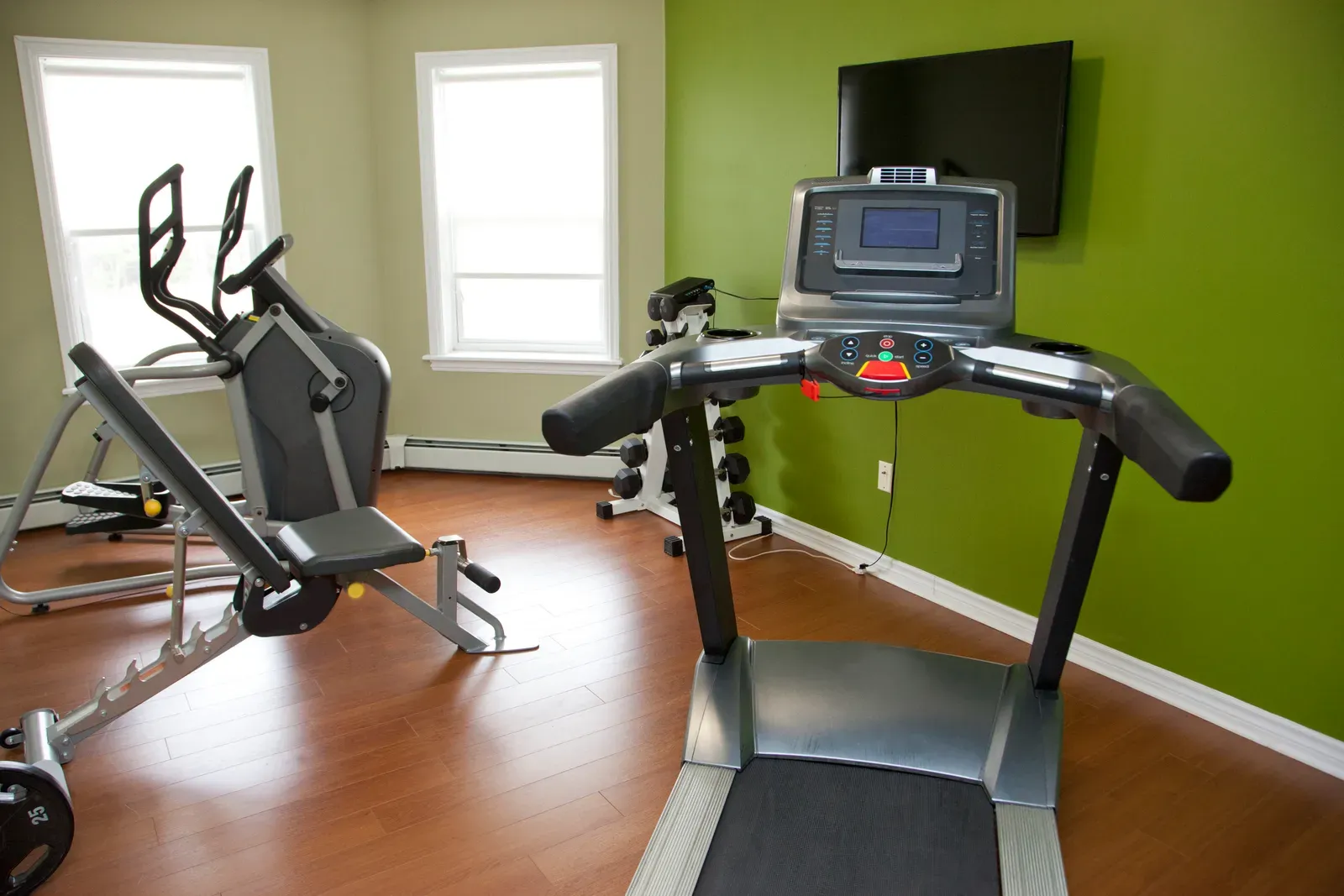 A compact apartment building fitness room with one treadmill and a dumbbell rack