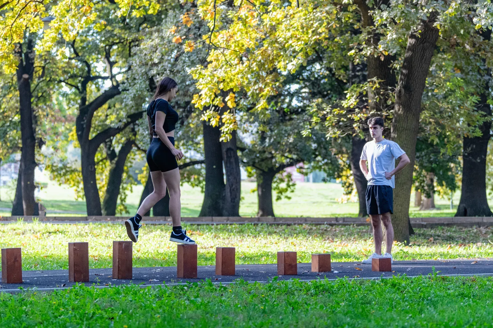 A couple working balance drills over wooden hurdles outdoors