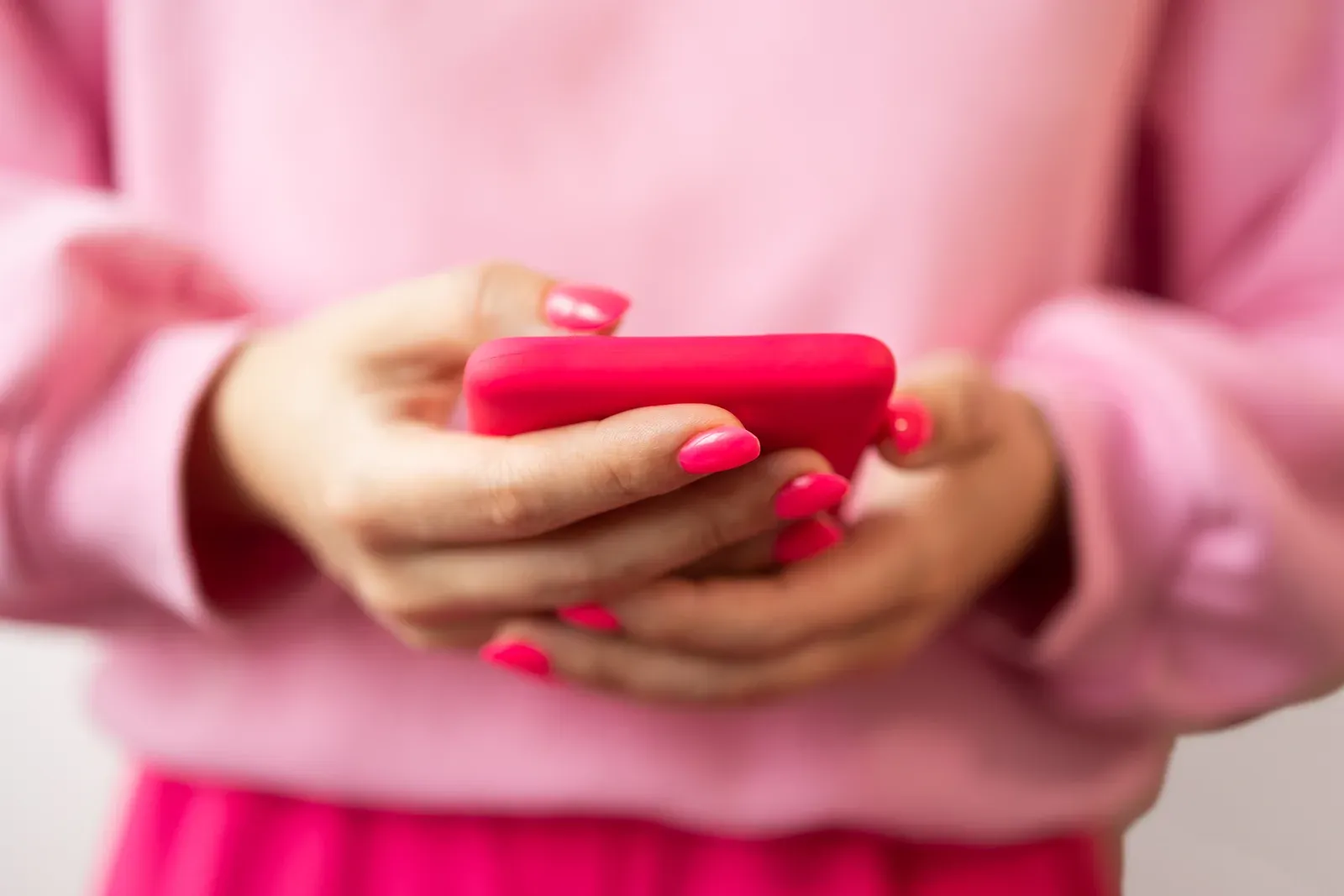 Woman with a pink manicure typing a message on her phone